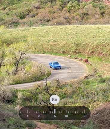 A blue classic car on a winding paved road through a green and brown hilly landscape