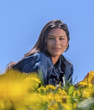 A woman lying in a field of yellow flowers, smiling at the camera