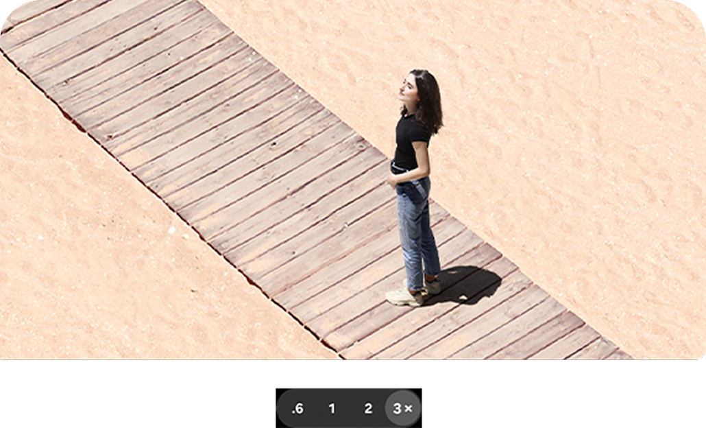 A woman standing on a beach walkway, zoomed into the 3x option.